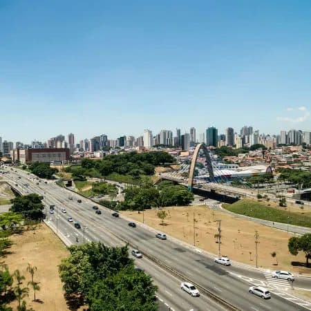 Vista panorâmica da cidade com rodovia e edifícios ao fundo sob céu azul