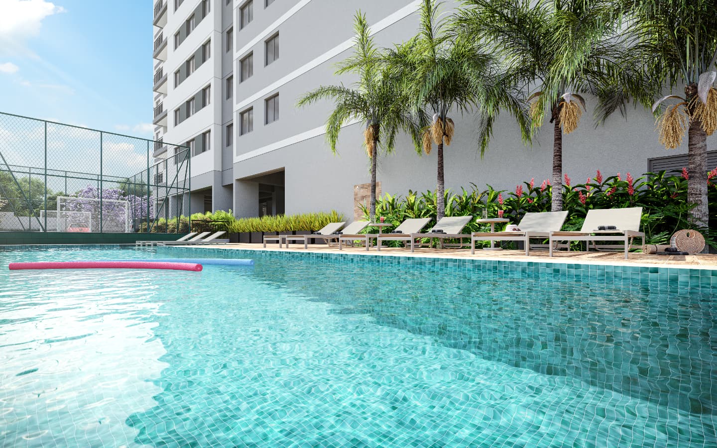 Piscina externa com espreguiçadeiras, palmeiras e quadra esportiva ao fundo.