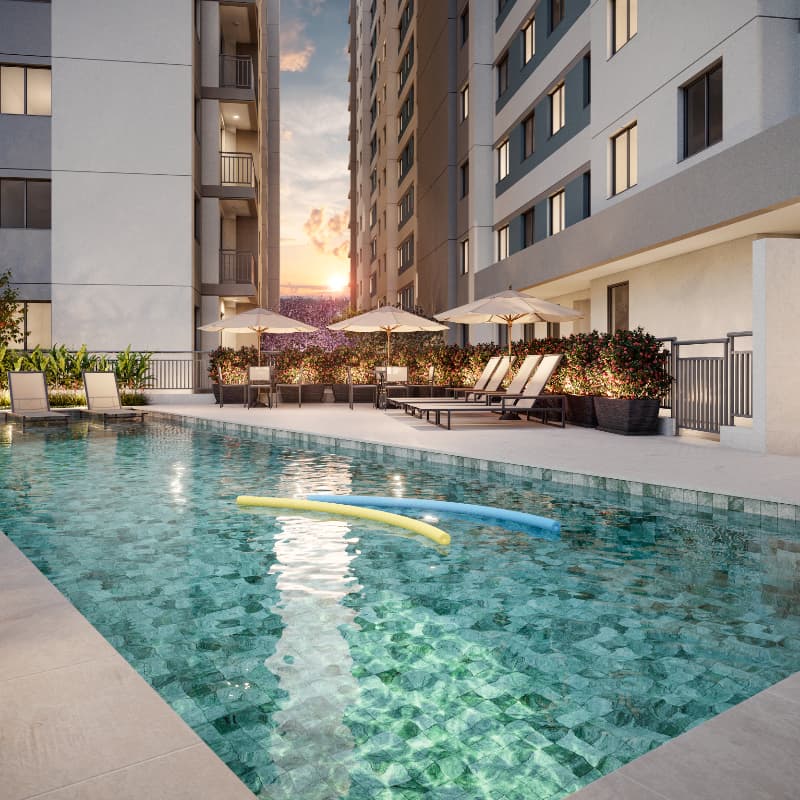 Área de lazer com piscina externa cercada por espreguiçadeiras e vegetação.